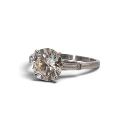 950/1000铂金单钻戒指，镶嵌一颗约2.5克拉的明亮式切割钻石，两侧各镶嵌一颗梯形切割钻石，总重