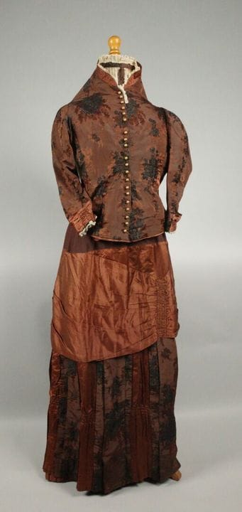 布雷斯。约1880-1885年间制作的里昂风格丝绸“翻褶”连衣裙。棕色底纹的锦缎面料上饰有黑色花束图