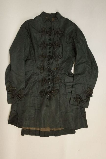 大衣，约1880年。黑色真丝面料，采用绳结式纽扣带和刻面纽扣闭合，配军官领，后背为平褶设计，饰有绳结
