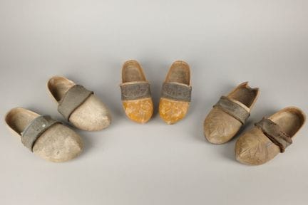 Drei Paar Holzclogs mit Lederbesatz am Schaft. 
Lä