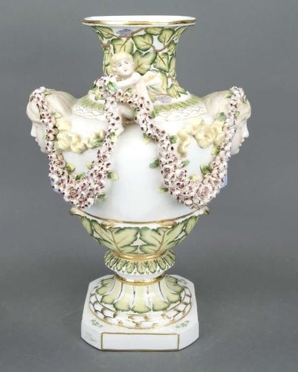装饰花瓶，20世纪末，双耳瓶造型，两侧把手呈女性头像，其间坐着手持玫瑰花环的立体小天使，彩绘并饰以镀