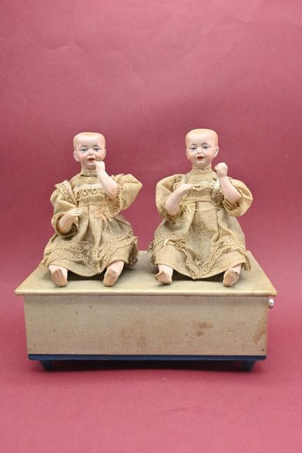 一款德国小型机械玩具，配有两个头部造型独特的“饼干人”婴儿，嘴巴紧闭，眼睛为手绘。
手摇式音乐装置。