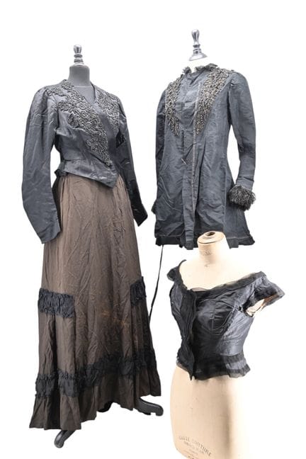 本套装包含：
- 1870年代的灰褐色真丝裙，配有黑色绉纱荷叶边。
- 一件约1870年的晚礼服上衣