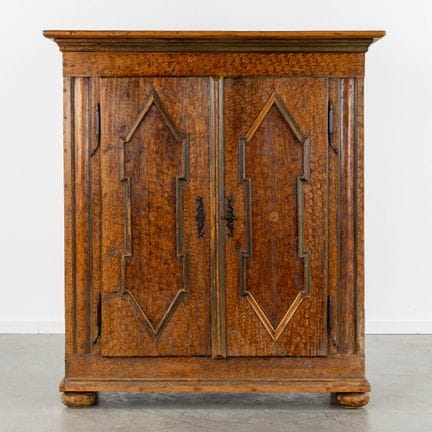 Ein zweitüriger Schrank auf Kugelfüßen, patinierte