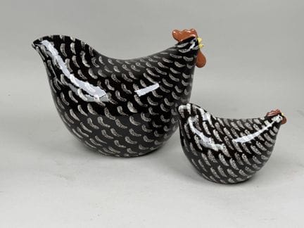Two decorative glazed terracotta hens on a brown b