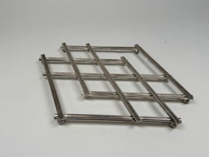 Folding silver plated metal trivet resting on smal