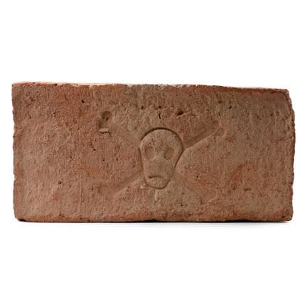 Brique médiévale en terre cuite ornée d’un crâne. 