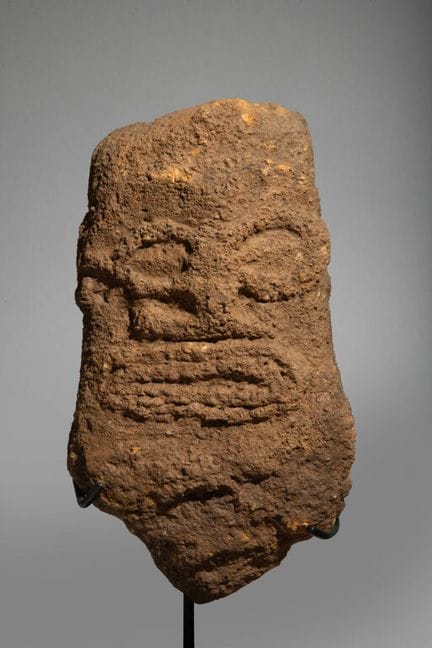 Skulptur, die einen Tiki-Kopf aus rötlichem Stein 