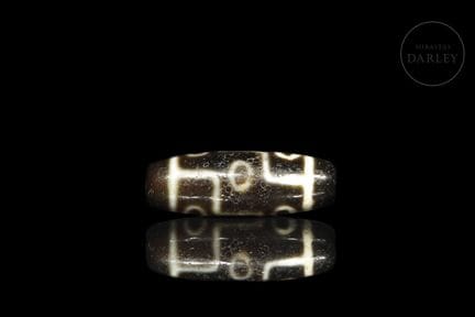 An elongated Dzi bead, crafted from brown agate wi