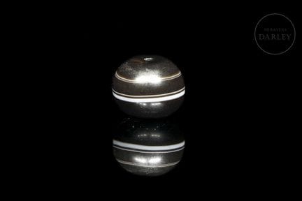 A spherical amulet carved from dark brown agate wi