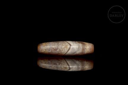 An elongated, spindle-shaped bead carved from natu