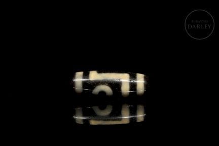 A tubular, barrel-shaped Dzi bead (གཟི།) made of a