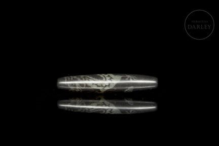 A large, fusiform, elongated bead carved from dark