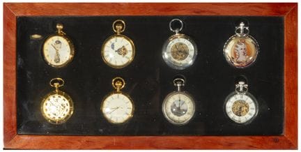Sammlung von acht Taschenuhren in einer Holzvitrin