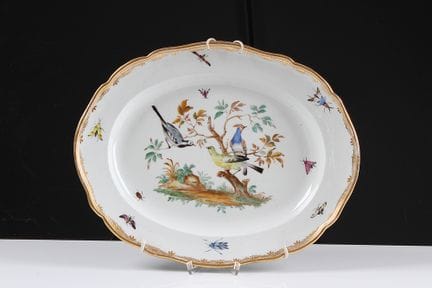 迈森瓷盘。马尔科利尼时期（1774—1814）。盘面中央为风景底纹，枝头栖息着各种鸟类。旗帜上描绘着