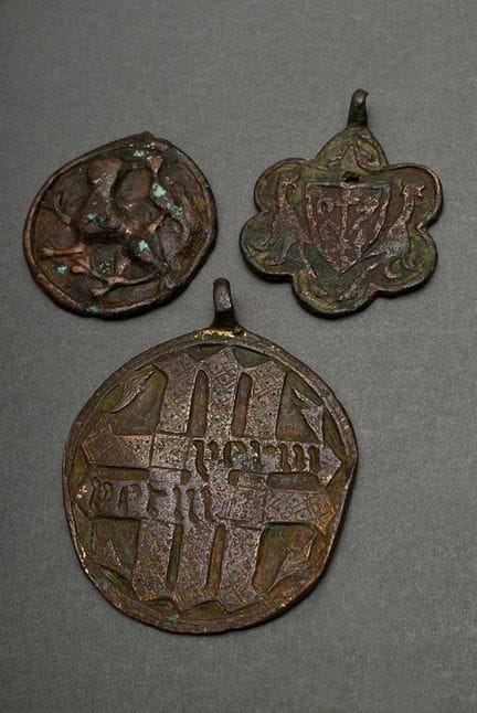 3 件中世纪青铜吊坠及金属配件，饰有“纹章”、“箴言带”以及“狮子与鸟”等不同浮雕图案，直径 4-6