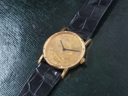 CORUM 10$
18K 黄金腕表。圆形表壳，侧面有凹槽。按扣底盖，自由女神面孔。
表盘由一枚 1