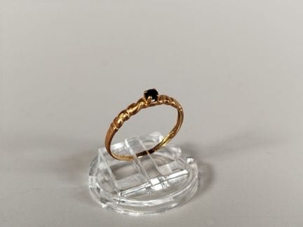 18K 750黄金戒指，戒圈两侧饰有交错纹样，中央镶嵌一颗深蓝色小圆形刻面宝石（很可能是蓝宝石），采