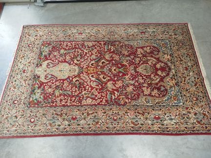 结点编织地毯，采用丝质纤维制成，红底上以对称构图呈现花瓶、花卉藤蔓及多彩鸟类图案，配以宽阔的象牙色边