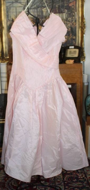 一件粉色的复古舞会礼服或晚礼服（1950年代至1980年代风格），采用V形低腰设计，配有交叉式露肩领