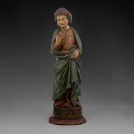 一件古色古香的多色木雕，刻画了一位身着红色短袍和绿色垂褶斗篷的年轻男圣徒。他右手高举，作祝福之势，左