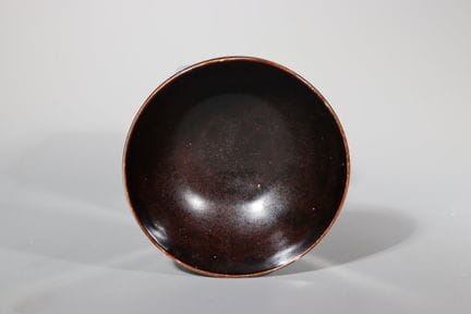 一件重要的定窑黑釉碗， 宋代。器形深圆，自短圆足部向上延伸至微微外翻的唇口，内外均覆有光泽的深褐黑色
