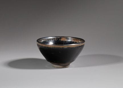 宋代建窑黑釉碗，碗身深而圆润，自短足处向上延伸至微微外翻的碗口，内外均覆有光泽黝黑的釉层，内壁呈现出