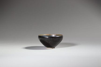 宋代郴州黑釉油斑碗，碗身深而圆润，自短足向上延伸至略微内收的碗口，通体覆以光泽黝黑的釉层，釉面遍布密