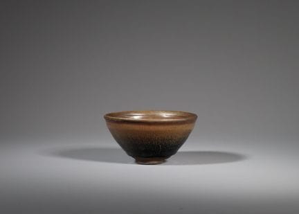 宋代建窑黑釉碗，碗身呈深锥形，自短足处向上延伸至略微外翻的碗口，内外均覆有光泽黝黑的釉层，釉面布满从