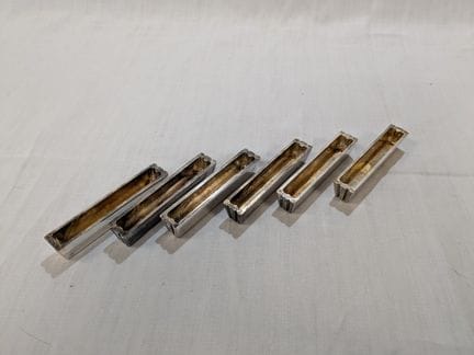 一套6个镀银的金属刀架，饰有条纹。长度：7.5厘米。