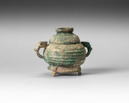 A covered bronze vessel with a green patina, shape