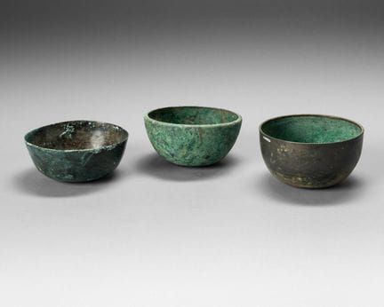 Tres cuencos de bronce, uno con pátina verde y los