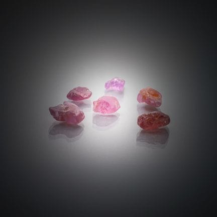 Set aus sechs rohen rosa Spinellen auf Papier. 
Vi