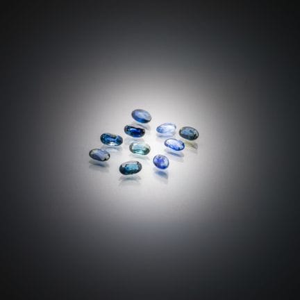 Set aus zehn ovalen blau-grünen Saphiren auf Papie