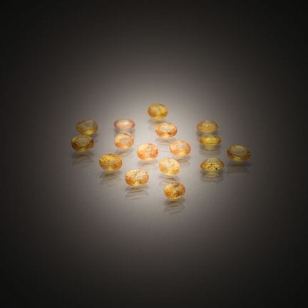 Set of sixteen oval yellow sapphires on paper.
Wei