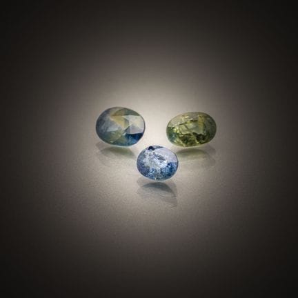Set of three oval blue/green sapphires on paper. 

