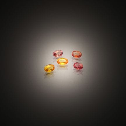 Set of five multicolored oval sapphires on paper.
