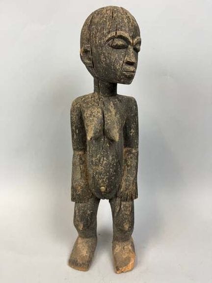 一尊木雕女性雕像，表面呈深色、风化且呈鳞片状，表现为站立姿态，可见干裂纹和使用痕迹。
科西德象牙，洛