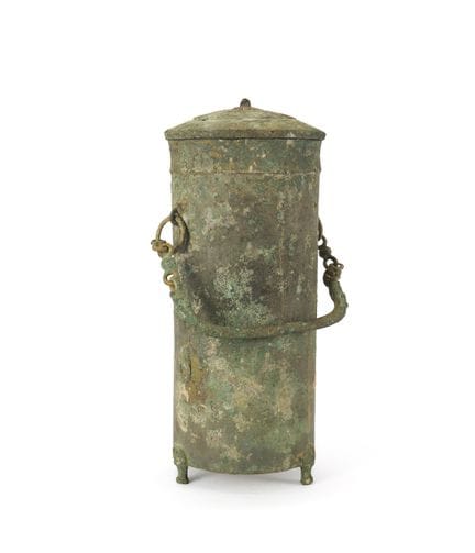 Un pequeño recipiente cilíndrico de bronce con asa