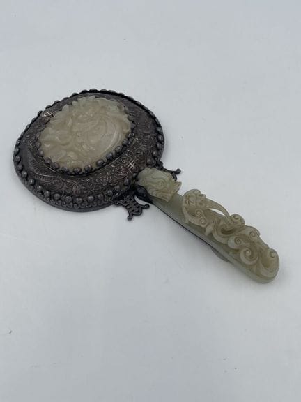 中国，嘉庆年间，
手持式，柄呈玑钗形，为青玉所制，饰有龙首扣，柄身雕有手持灵芝枝的蚕龙。 镜背镶嵌青