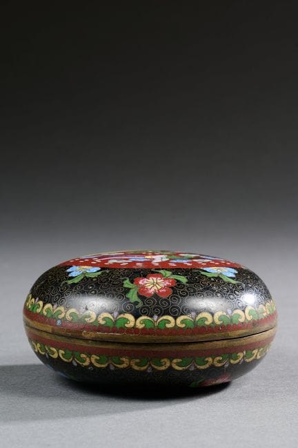 中国，约 1920 年 
铜胎掐丝珐琅有盖小圆盒，卷轴背景上有扇子和花朵的多色装饰。 
直径：9 厘