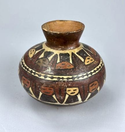 纳斯卡 - 秘鲁 - 公元400-600年
饰有战利品人头图案的球形花瓶。这些图案以棕色为底，分两层