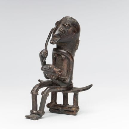 加纳，阿坎族，一件铜合金雕塑，刻画了一位坐姿的猎人，右手持剑，左手握着一个动物头颅。高9.5厘米。[