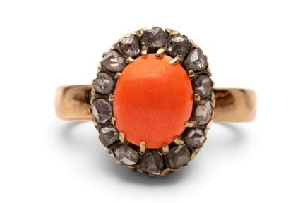 A coral and diamond ring set with an oval cabochon