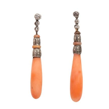 A pair of coral drop earrings. Above the pinkish c
