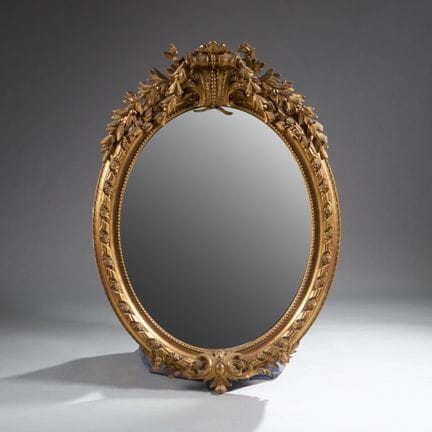 A large oval beveled mirror with a wooden frame an