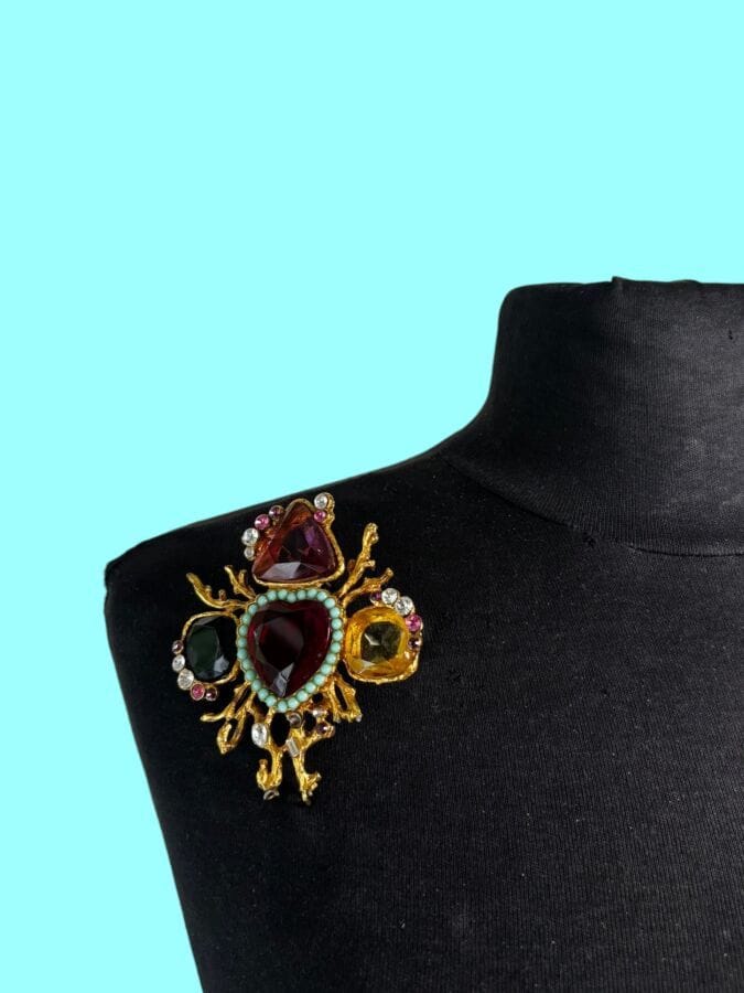 CHRISTIAN LACROIX Made in France Broche baroque en métal doré pierres taillées de couleur petits cabochons de verre turquoise et strass pampille en cristal transparent  - signée
Ht : 12 cm
(manque un strass)
