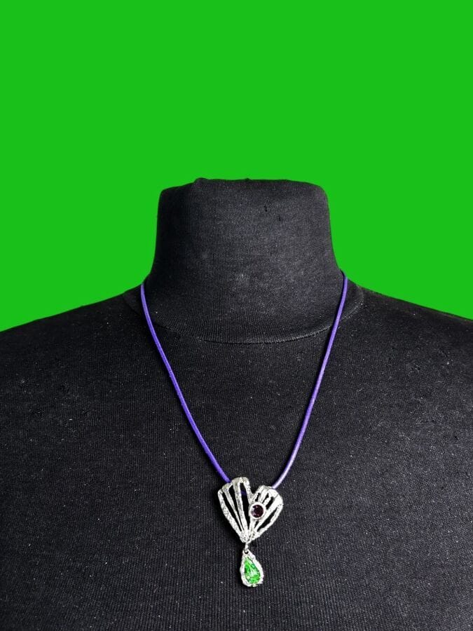CHRISTIAN LACROIX Made in France Openwork silver-patina metal heart pendant with green and purple rhinestones—signed, mounted on a purple leather cord
4 x 2.5 cm