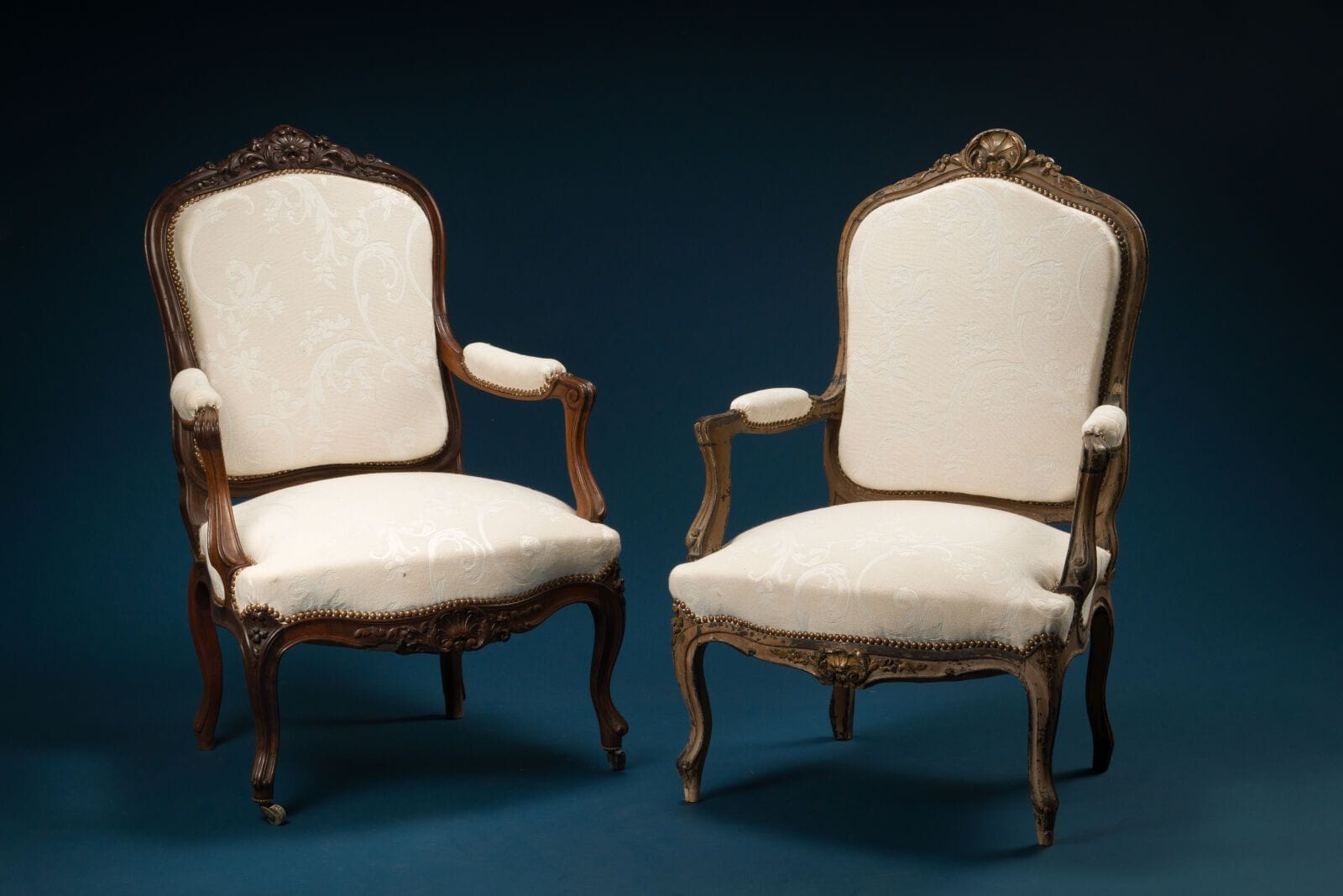 A set of two armchairs with flat backs, one in natural wood and the other formerly lacquered, featuring carved decorations of shells and small flowers, curved legs, and upholstered in white fabric. 
Louis XV style
H.: 102 cm; W.: 69 cm; D.: 69 cm.