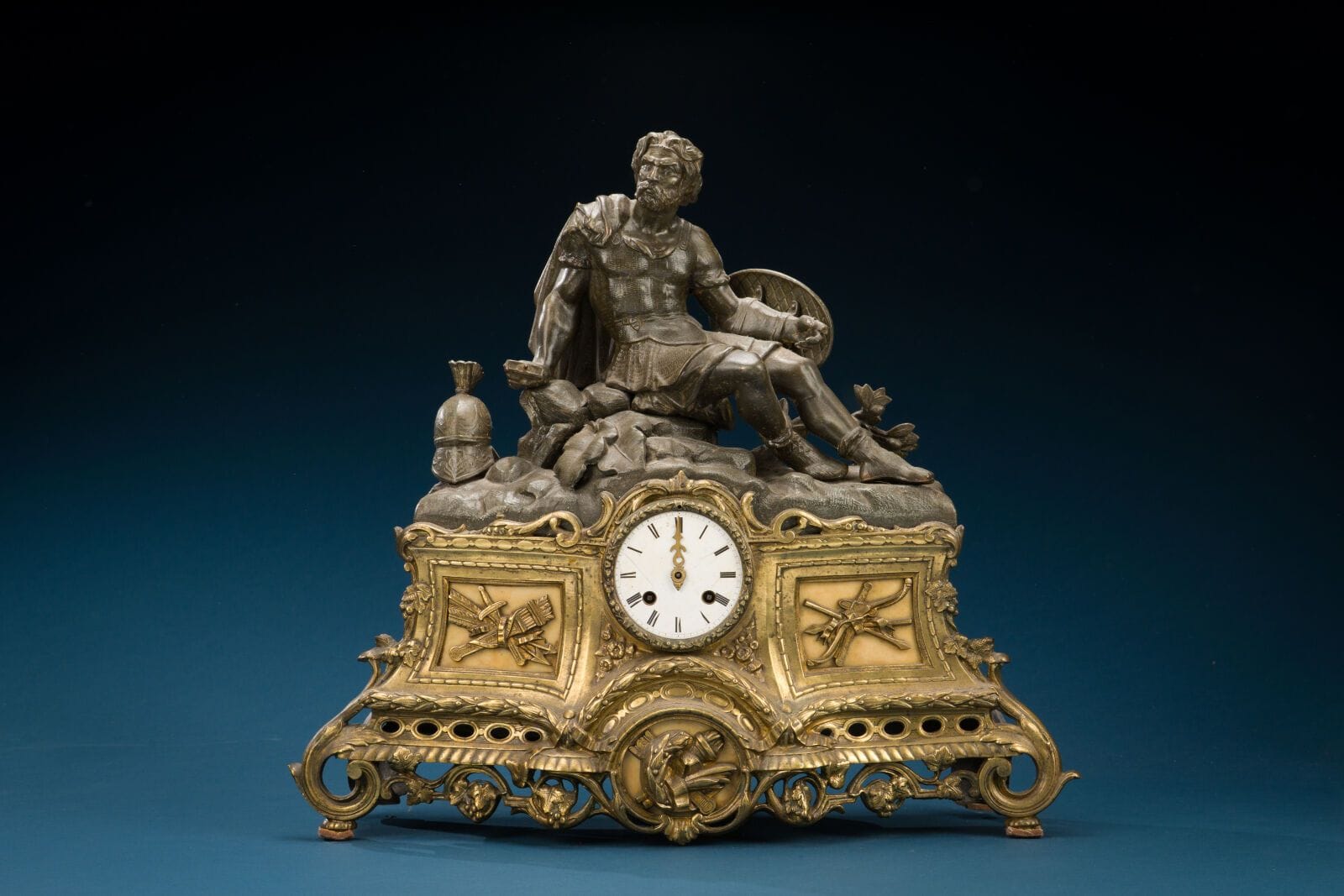 Large gilded metal clock with a Spartan-style decoration, mid-19th century 
(Sword missing, legs damaged)
47 x 49 cm.